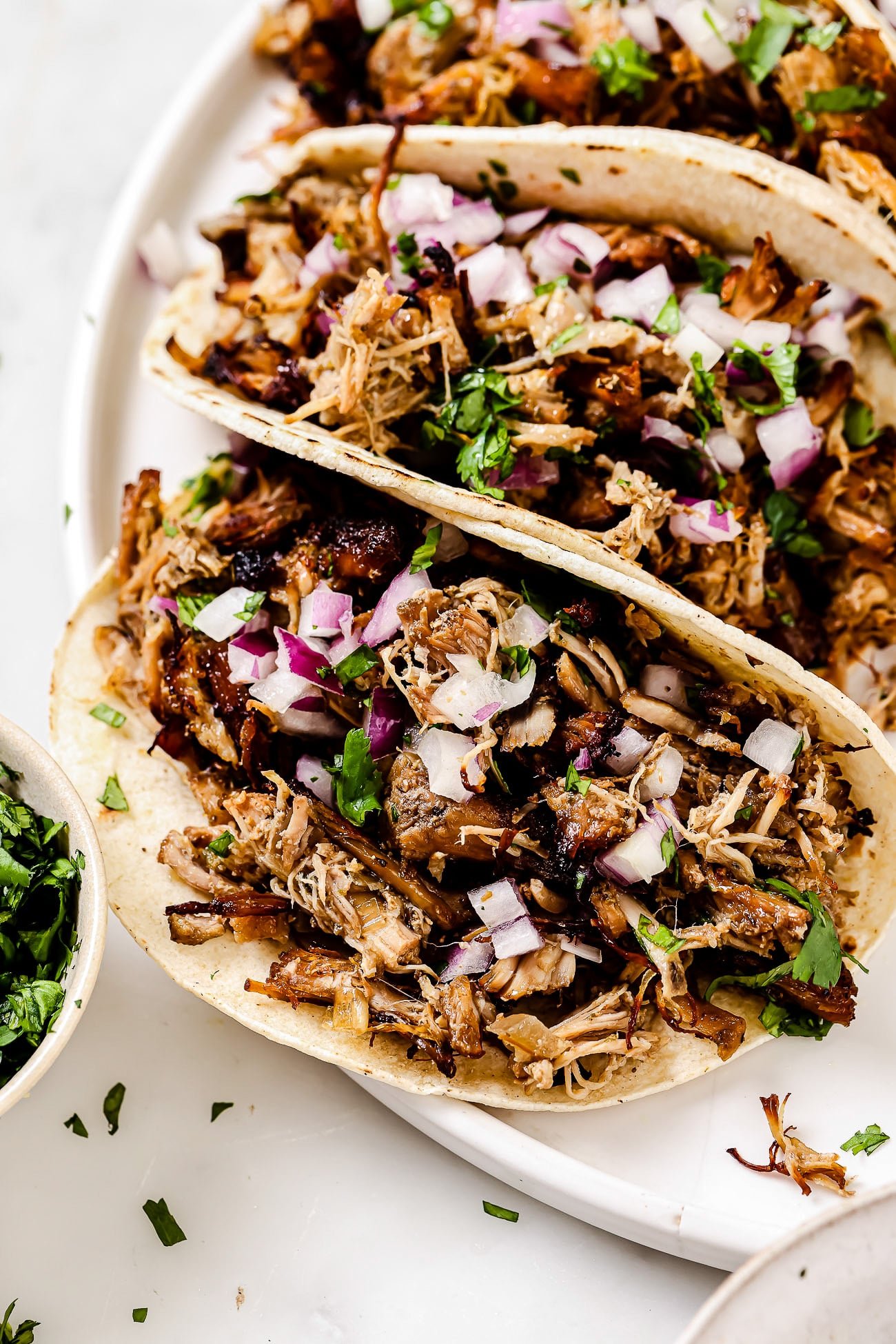 An overhead view of carnitas tacos topped with onion and cilantro on a white plate.