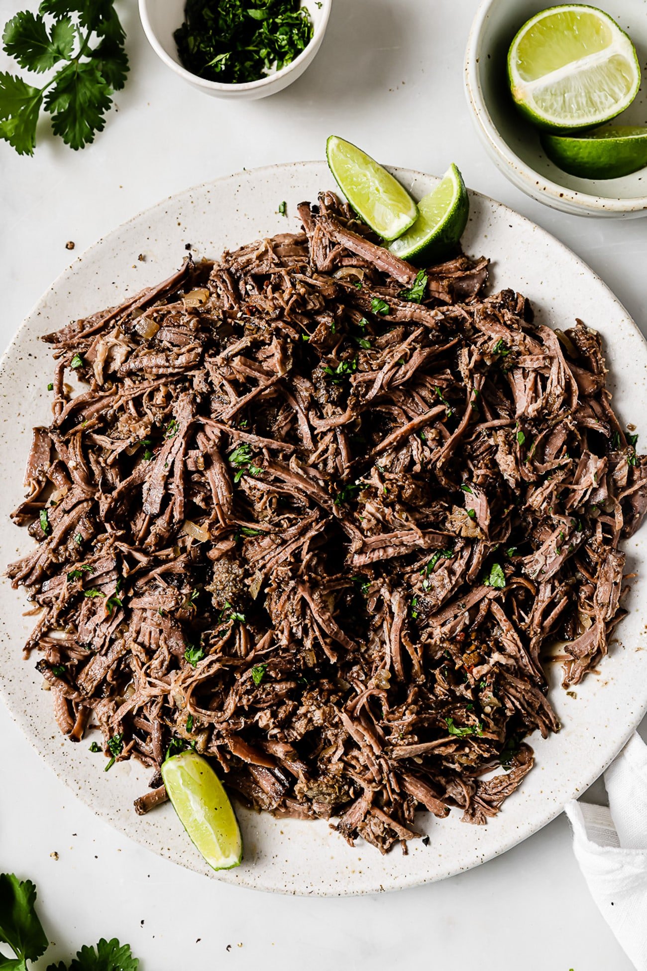 Slow-cooker barbacoa on a serving platter garnished with cilantro and lime wedges. 
