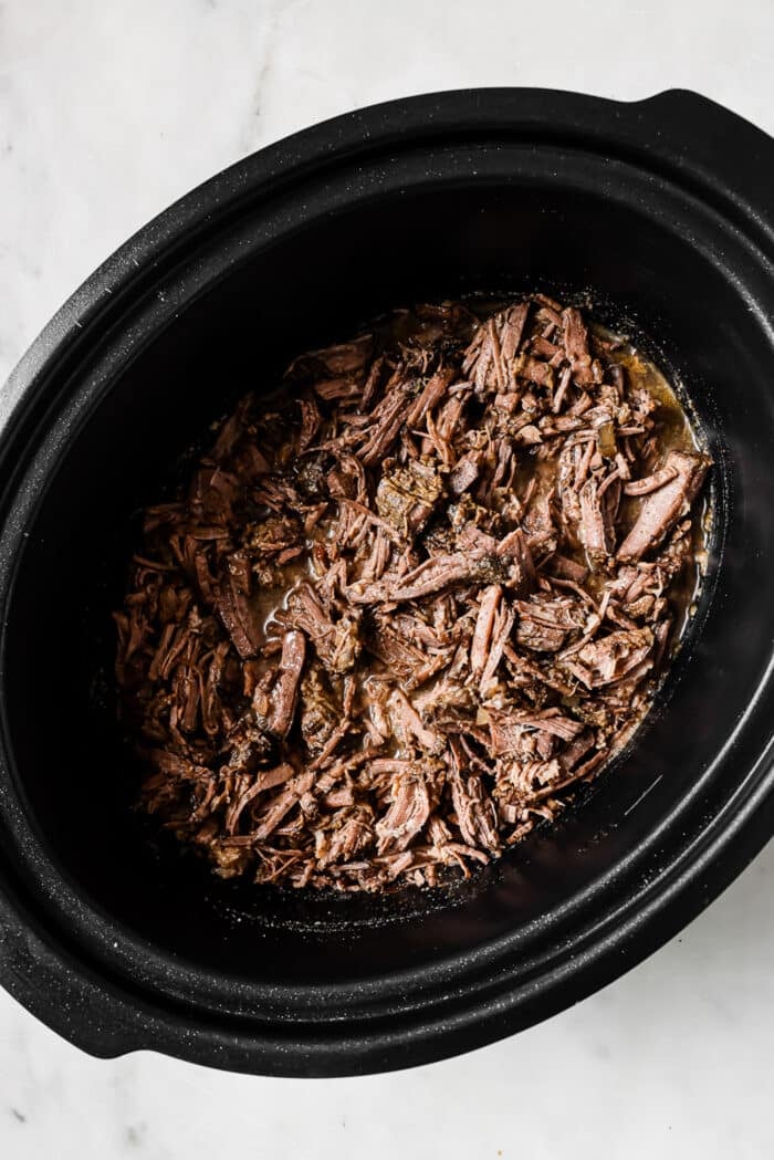 The shredded barbacoa is placed back in the crockpot.