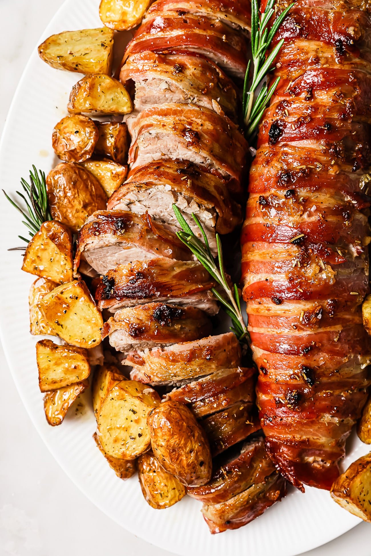 An overhead view of bacon-wrapped pork tenderloin with roasted potatoes. 