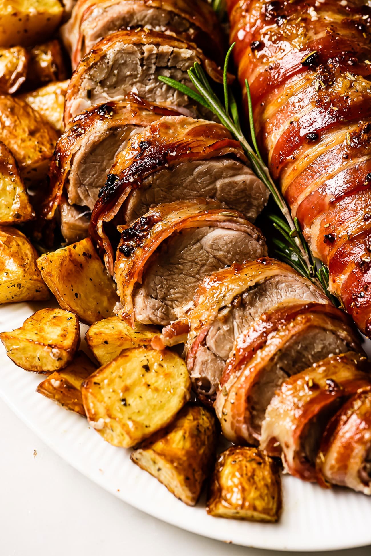 Sliced pork tenderloin on a serving dish with roasted potatoes on the side. 