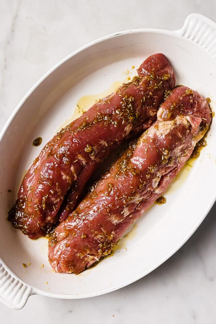 Two seasoned pork tenderloins in a white roasting dish. 