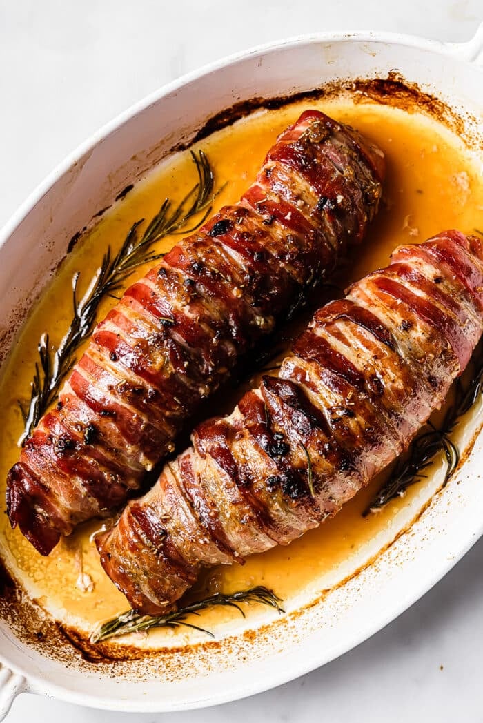 An overhead view of two roasted pork tenderloins wrapped in back. 