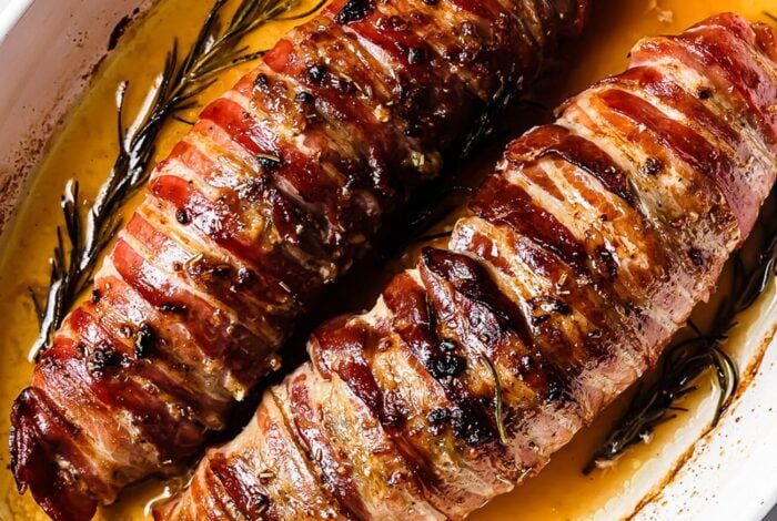 Two Bacon Wrapped Pork Tenderloins are roasted with rosemary and savory juices, resulting in a golden, crispy exterior and mouthwatering flavor.