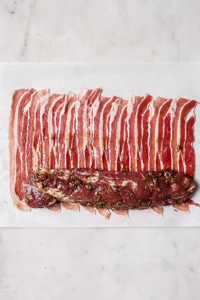A tenderloin laying on top of several strips of bacon. 