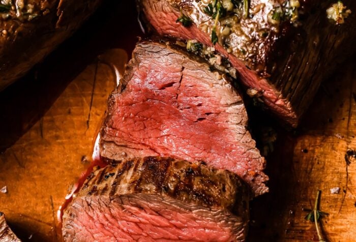 Garlic Butter Beef Tenderloin sliced medium-rare on a wooden cutting board, topped with a savory garlic and herb mixture. The beef is juicy and pink inside with a beautifully browned exterior.