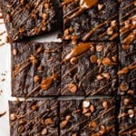 Nine Pumpkin Brownies are topped with chocolate chips and drizzled with melted chocolate, arranged on parchment paper.