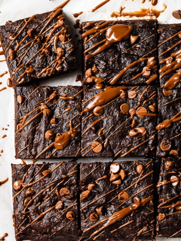 Nine Pumpkin Brownies are topped with chocolate chips and drizzled with melted chocolate, arranged on parchment paper.