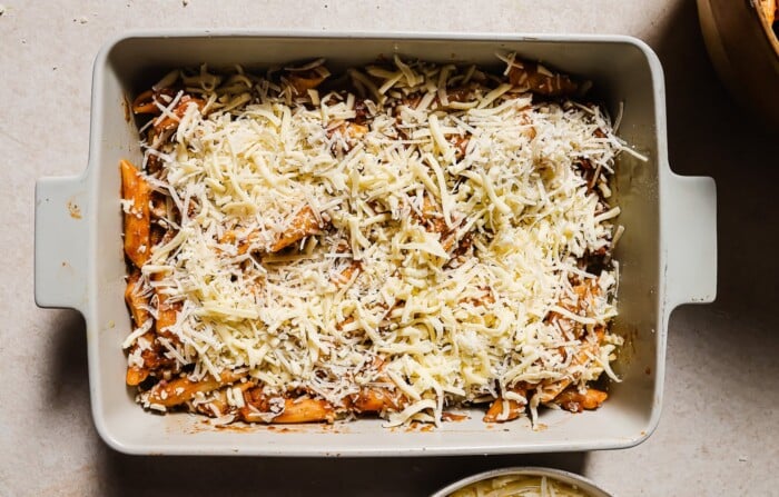 A rectangular baking dish filled with pasta, covered in rich tomato sauce and generously topped with shredded cheese, ready to be baked.