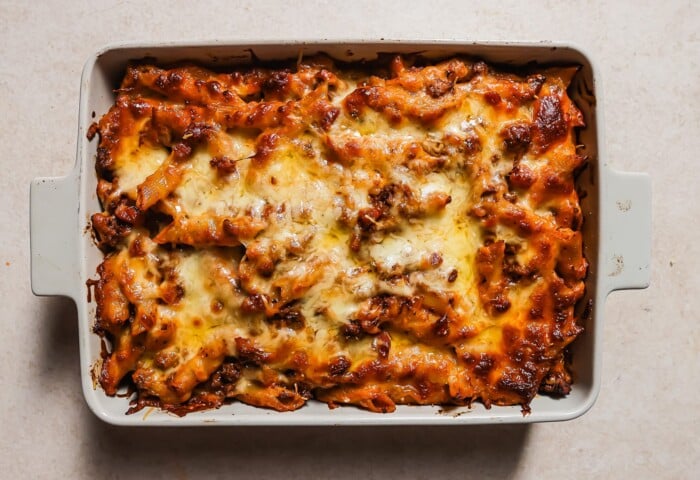 A rectangular baking dish filled with ziti pasta topped with melted, golden-brown cheese and a tomato-based sauce, sits on a light-colored surface.