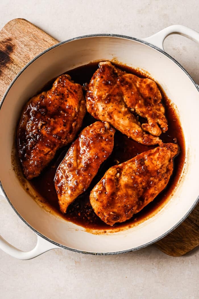 Honey garlic chicken breasts covered in sauce in a white skillet. 