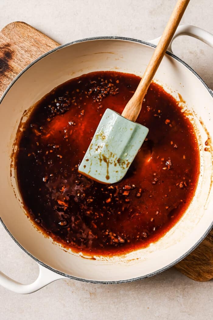 Sticky honey garlic sauce in a white skillet with a blue rubber spatula in it. 