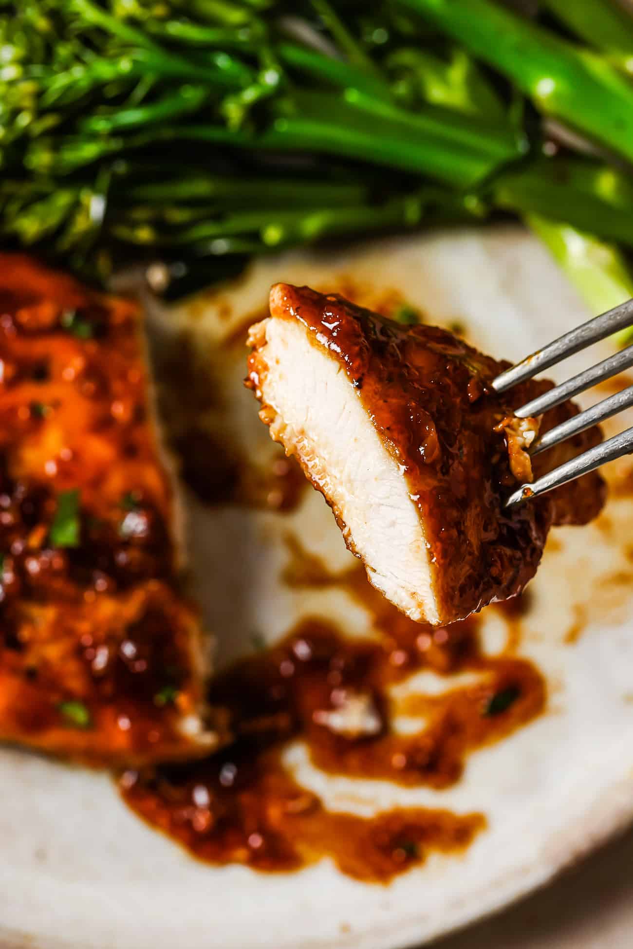 A piece of honey garlic chicken breast on the tip of a fork. 