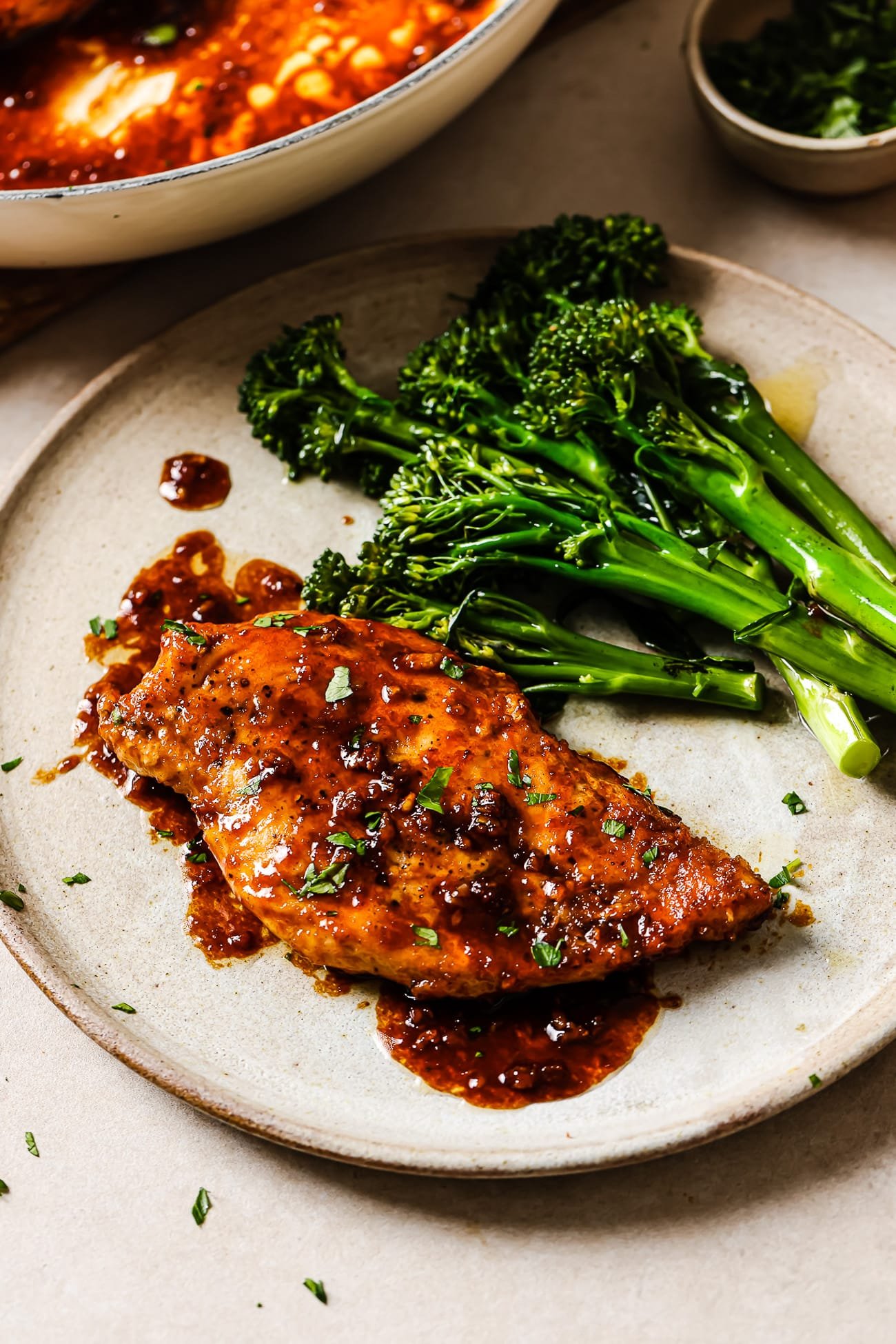 Honey garlic chicken breast on a white plate with a side of broccolini. 