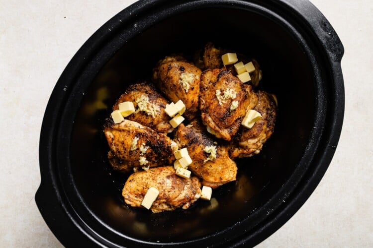 chicken thighs inside of a slow cooker with butter in top