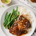 Slow Cooker chicken thighs on a white plate with green beans and rice.