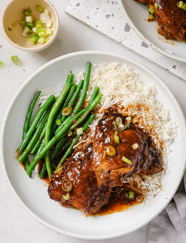 Slow Cooker chicken thighs on a white plate with green beans and rice.