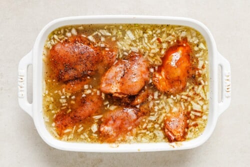 raw chicken thighs in a white casserole with raw rice