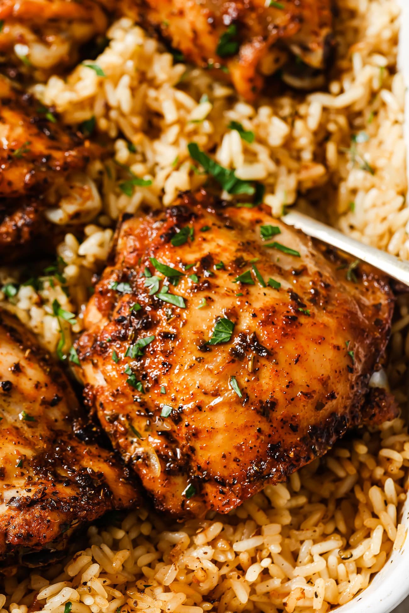 A closeup of baked chicken thighs over rice in a white baking dish.