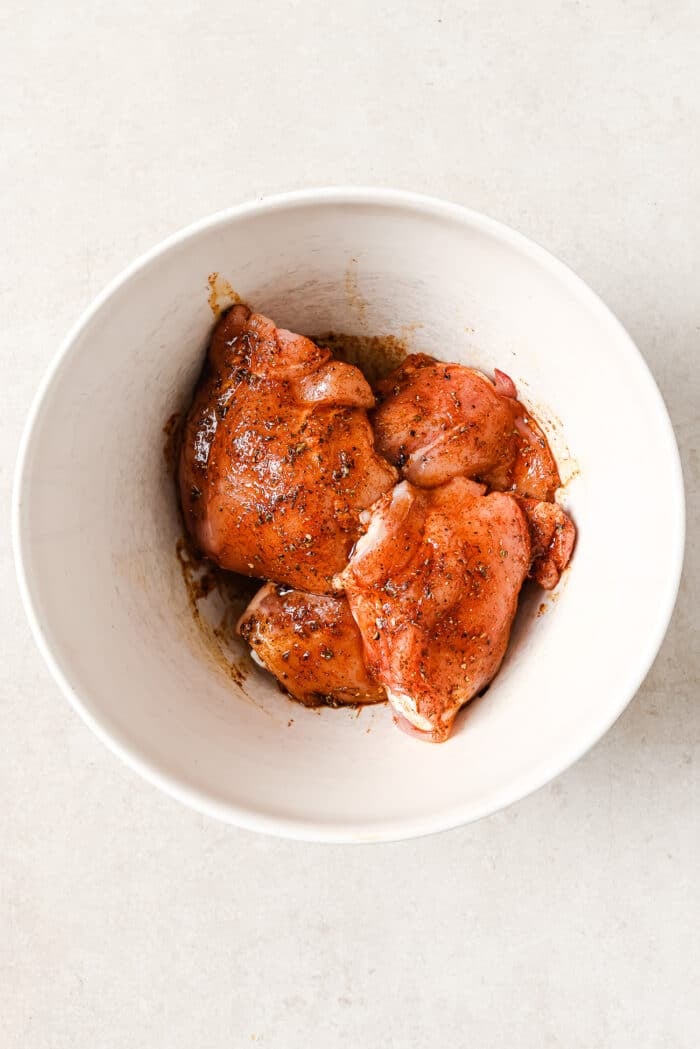 An overhead view of marinated chicken thighs in a white serving bowl.