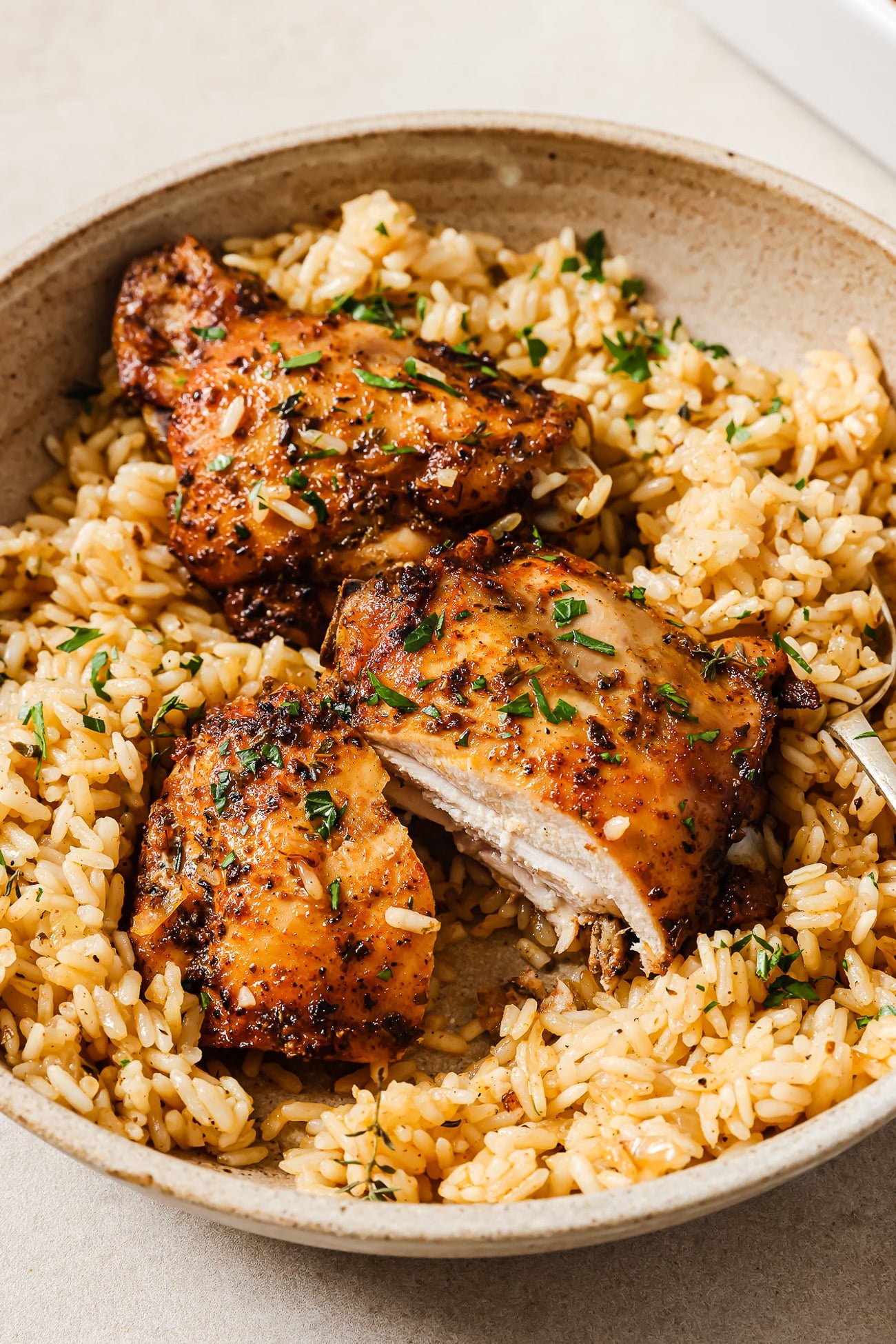 Two baked chicken thighs over rice, garnished with parsley, in a serving bowl.