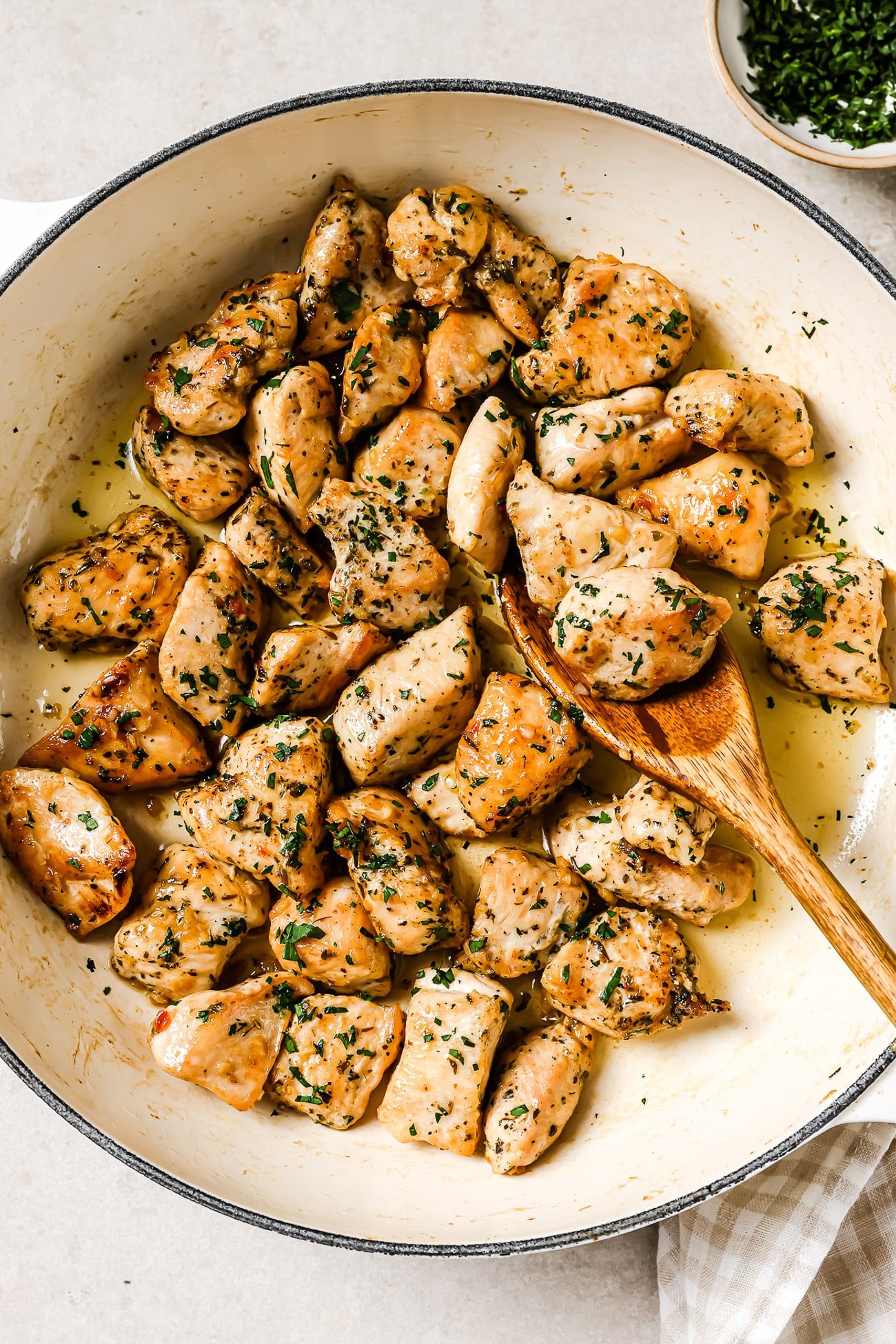 An overhead view of garlic butter chicken bites in a skillet with a wooden spoon in it.