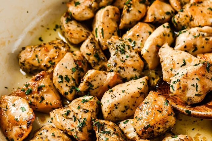 A white skillet filled with browned, bite-sized pieces of Garlic Butter Chicken Bites, seasoned with herbs and garnished with chopped parsley. The chicken appears juicy and freshly cooked.