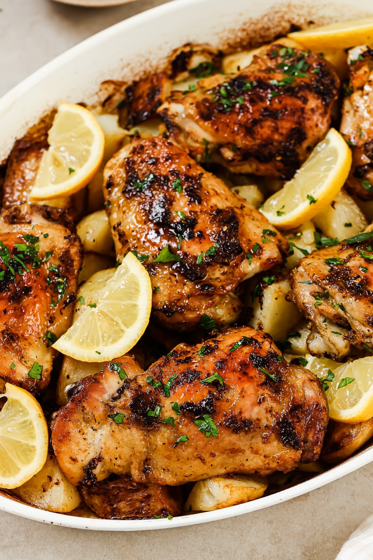 Greek chicken and potatoes garnished with lemon wedges and fresh parsley in a white baking dish.