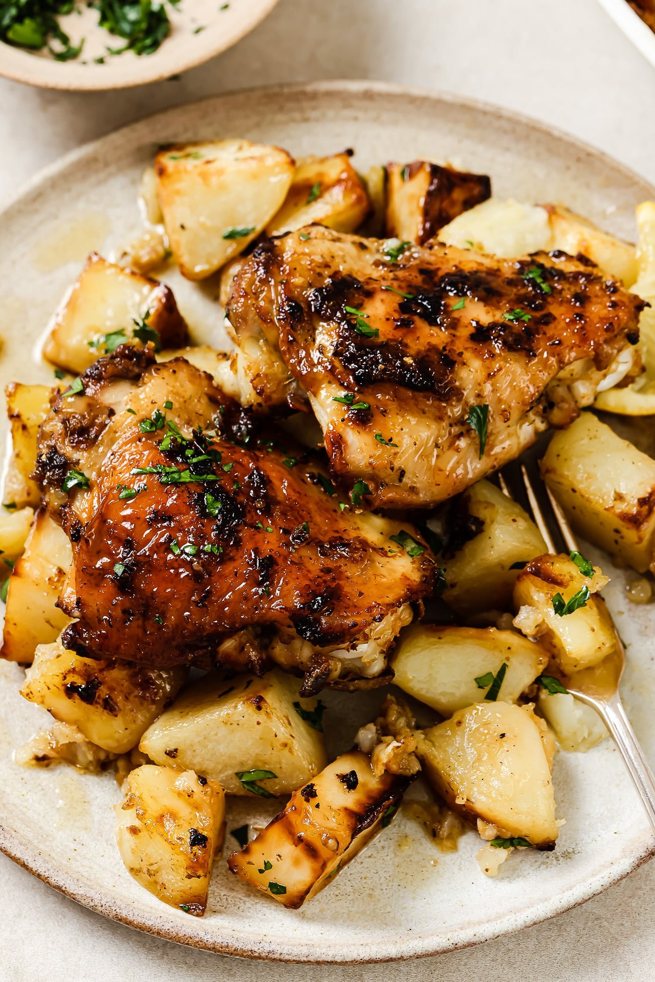 Two Greek chicken thighs over a bed of roasted potatoes on a white plate.