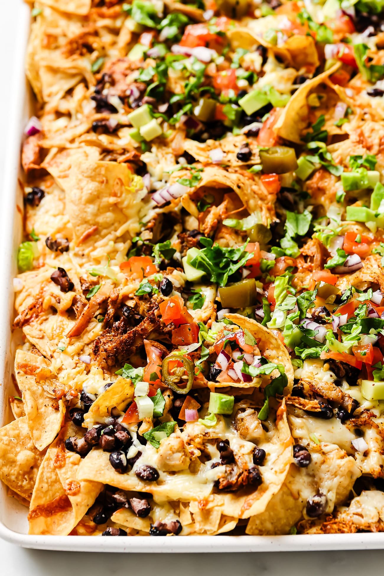 An overhead view of rotisserie chicken nachos with jalapenos, cilantro, avocado, and pico de gallo. 