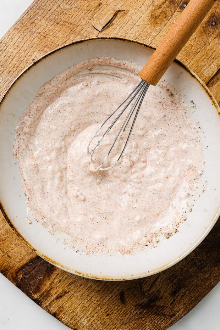 Greek yogurt marinade in a white bowl with a whisk in it. 
