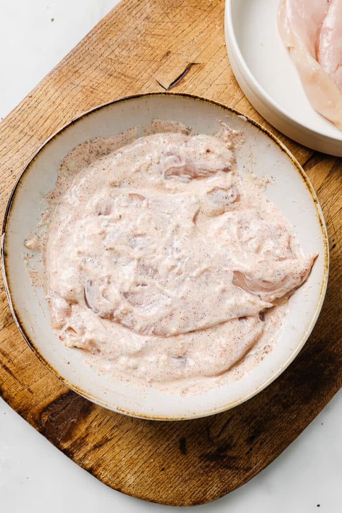 Chicken breasts coated in yogurt marinade arranged on a large serving plate. 