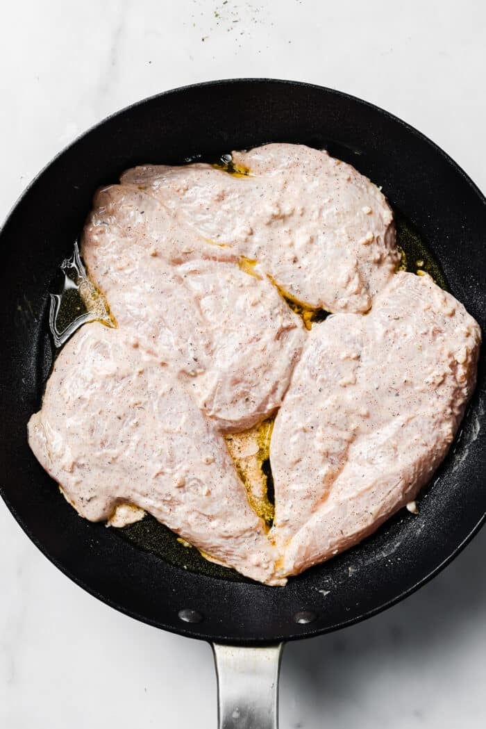Four yogurt-marinated chicken breasts in a hot skillet. 