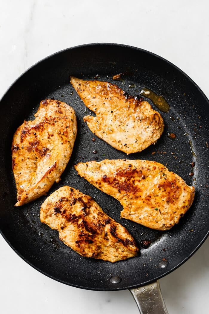 Four yogurt-marinated chicken breasts searing in a large skillet. 