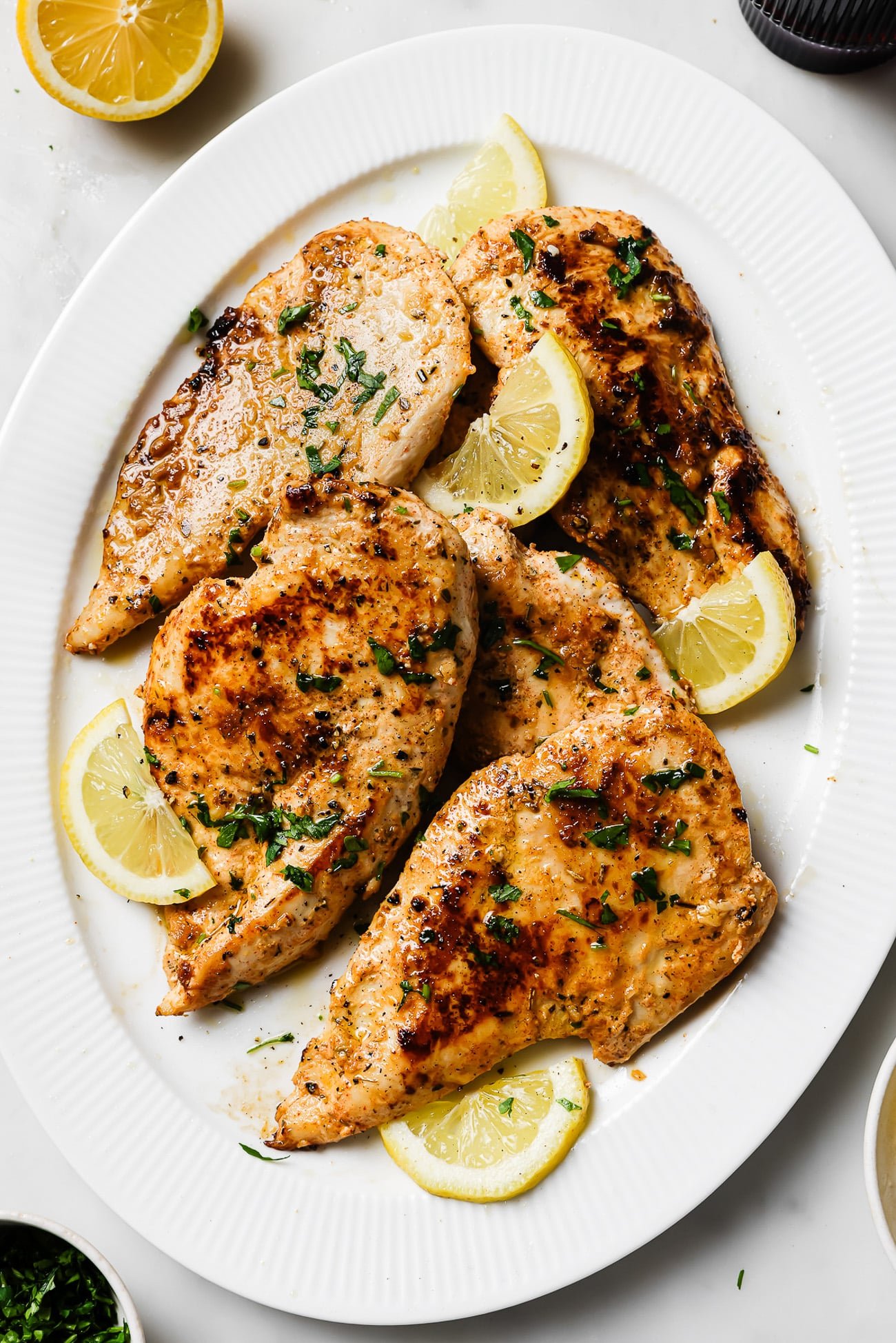 Yogurt-marinated chicken breasts garnished with lemon slices and parsley on a white serving dish. 