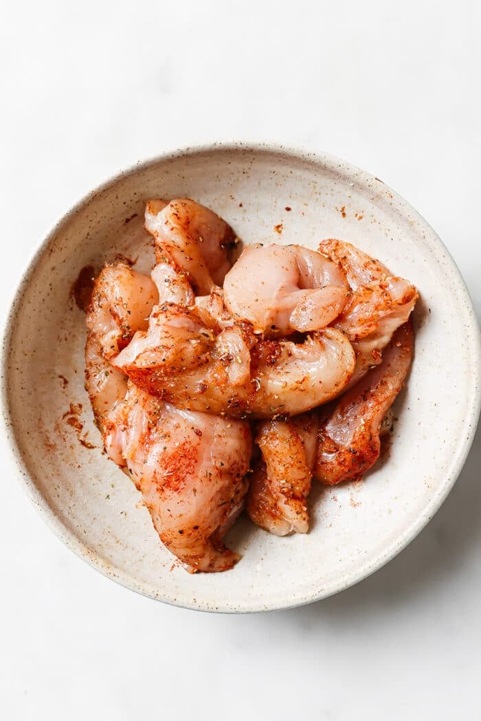 An overhead view of seasoned chicken tenders in a large mixing bowl.