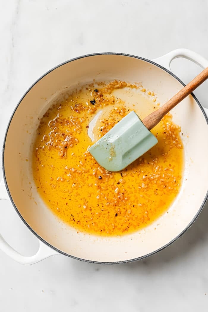 A large ceramic cast-iron pan with a blue spatula, butter, and garlic in it.