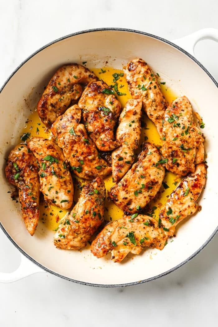 Garlic butter chicken tenders garnished with parsley in a ceramic cast-iron skillet.