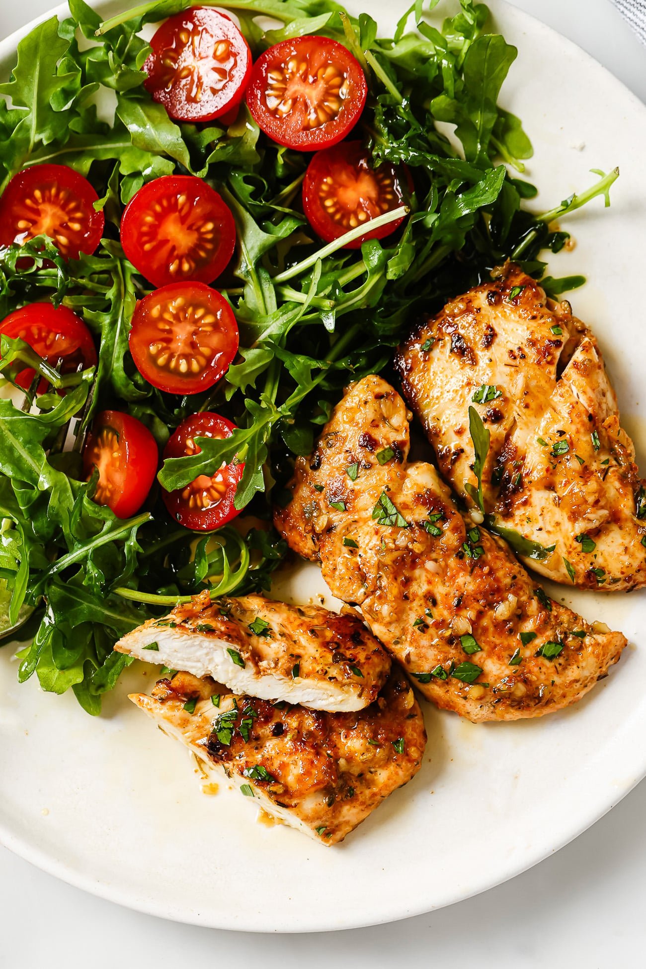 Garlic butter chicken tenders next to a side salad on a white plate.