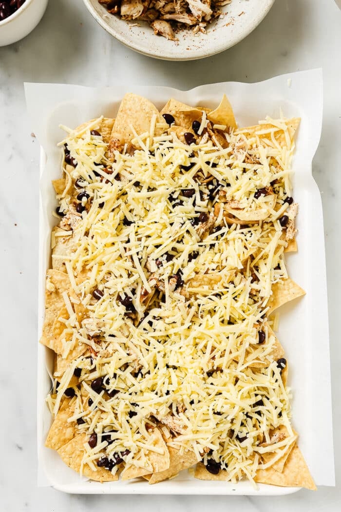 An overhead view of rotisserie chicken nachos on a sheet pan before going into the oven. 
