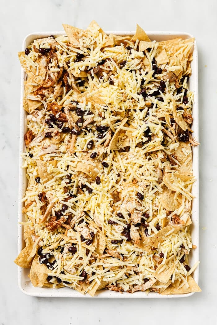 An overhead view of layered sheet pan nachos before going into the oven. 