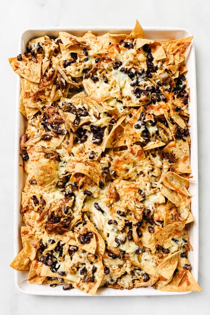 Rotisserie chicken nachos with melted cheese on a sheet pan.  