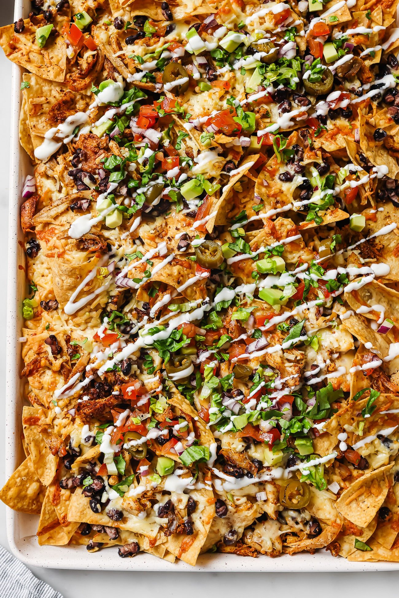 An overhead view of loaded rotisserie chicken nachos with sour cream, cilantro, and pico de gallo. 