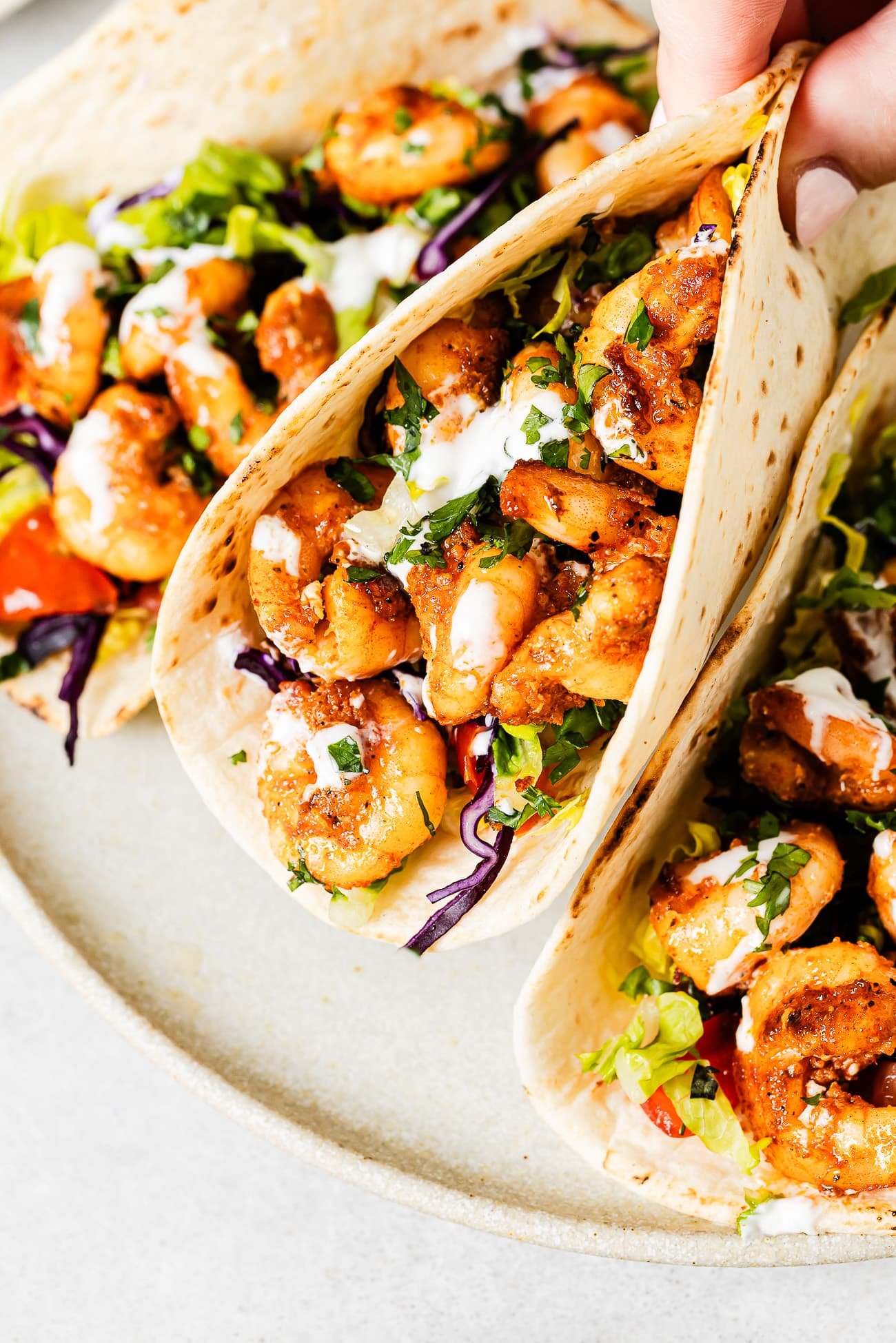 Three loaded shrimp tacos on a white serving plate.