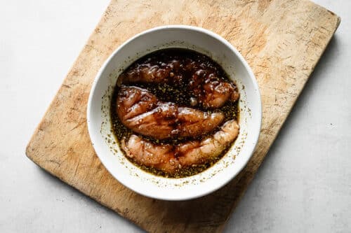 Balsamic marinade and raw chicken breast in a white bowl.