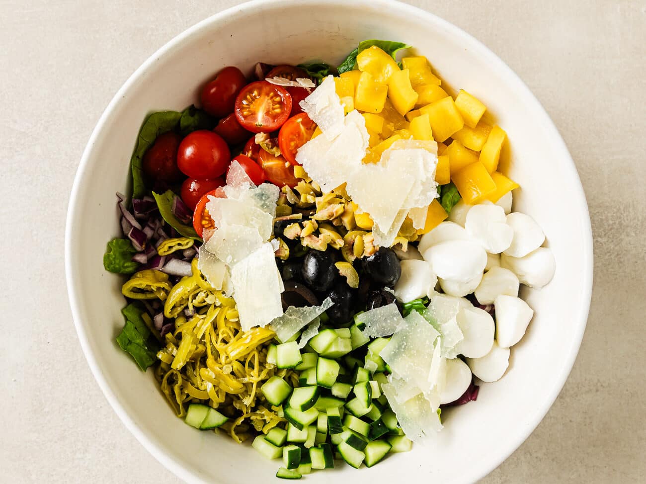 Italian chopped salad ingredients are arranged into piles on a base of lettuce in a large serving bowl.