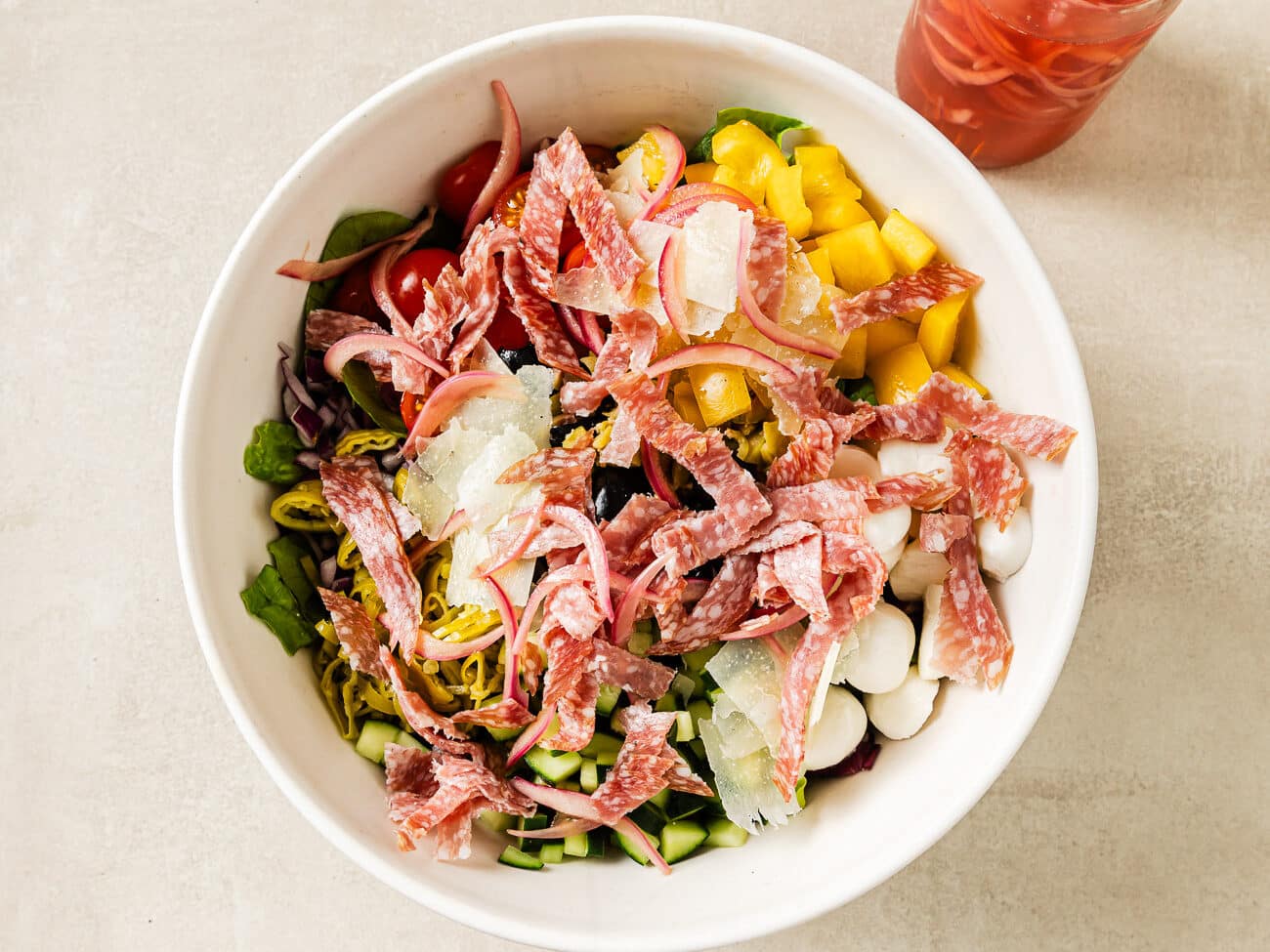 Sliced salami and pickled red onions are scattered on top of the other salad ingredients.
