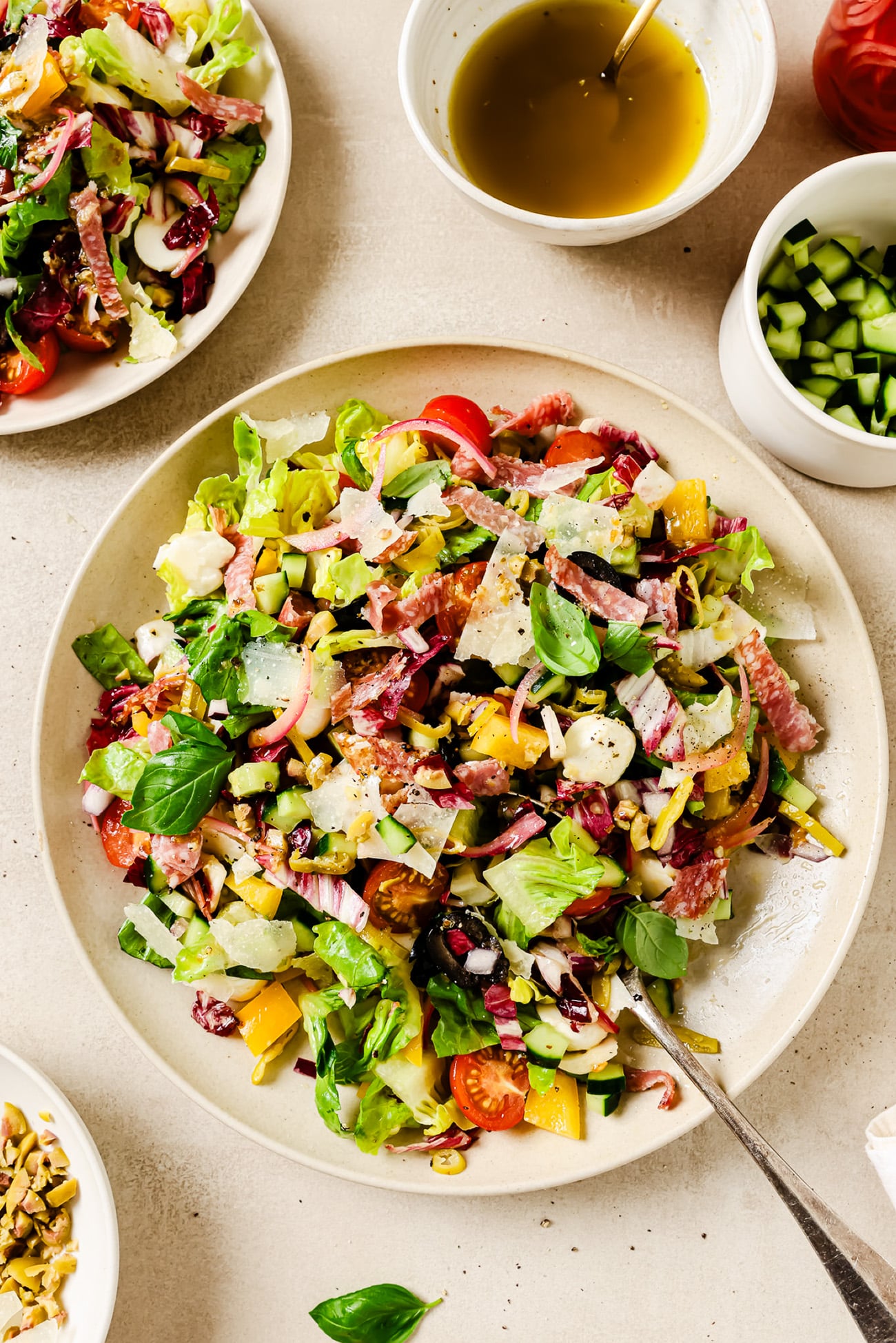 An overhead view of an Italian chopped salad with dressing and bowls of ingredients on the side.