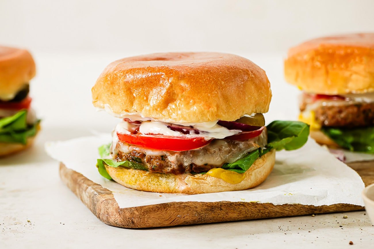 A side view of three ground turkey burgers with toppings and cheese.