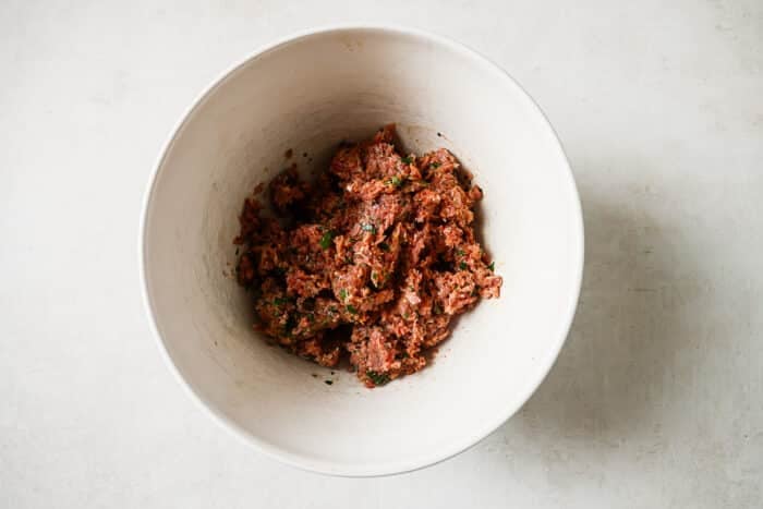 Ground turkey and spices mixed together in a large white bowl.